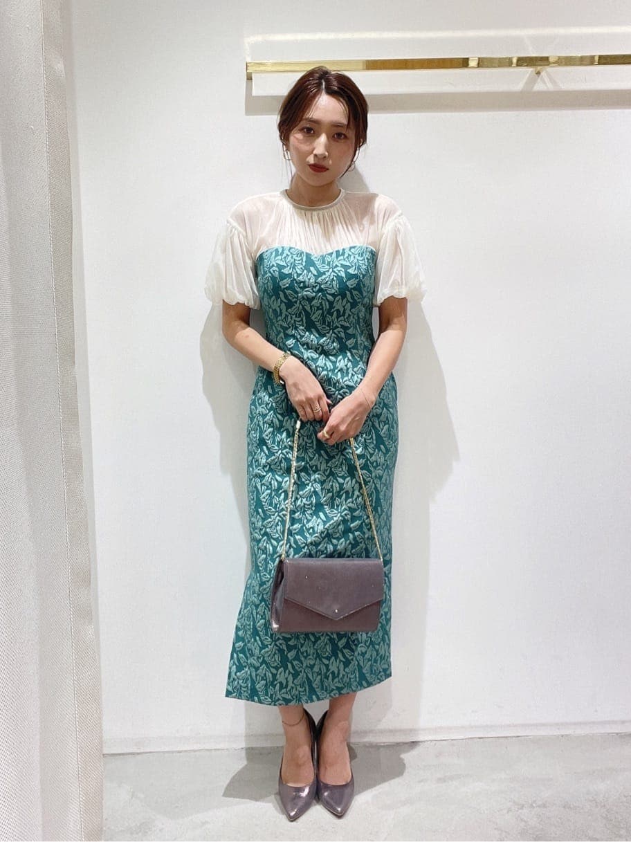 シルバー系のクラッチバッグ、シルバー系のパンプス、グリーン系のドレスを着用したレディースの秋コーディネートの3枚目の写真