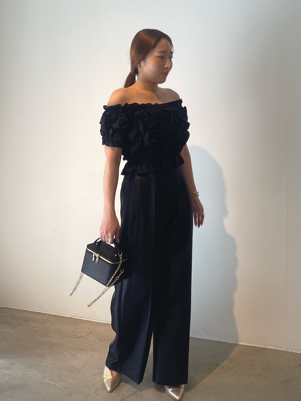 ブラック系のハンドバッグ、ゴールド系のパンプス、ブラック系のパンツドレスを着用したレディースの春コーディネートの3枚目の写真