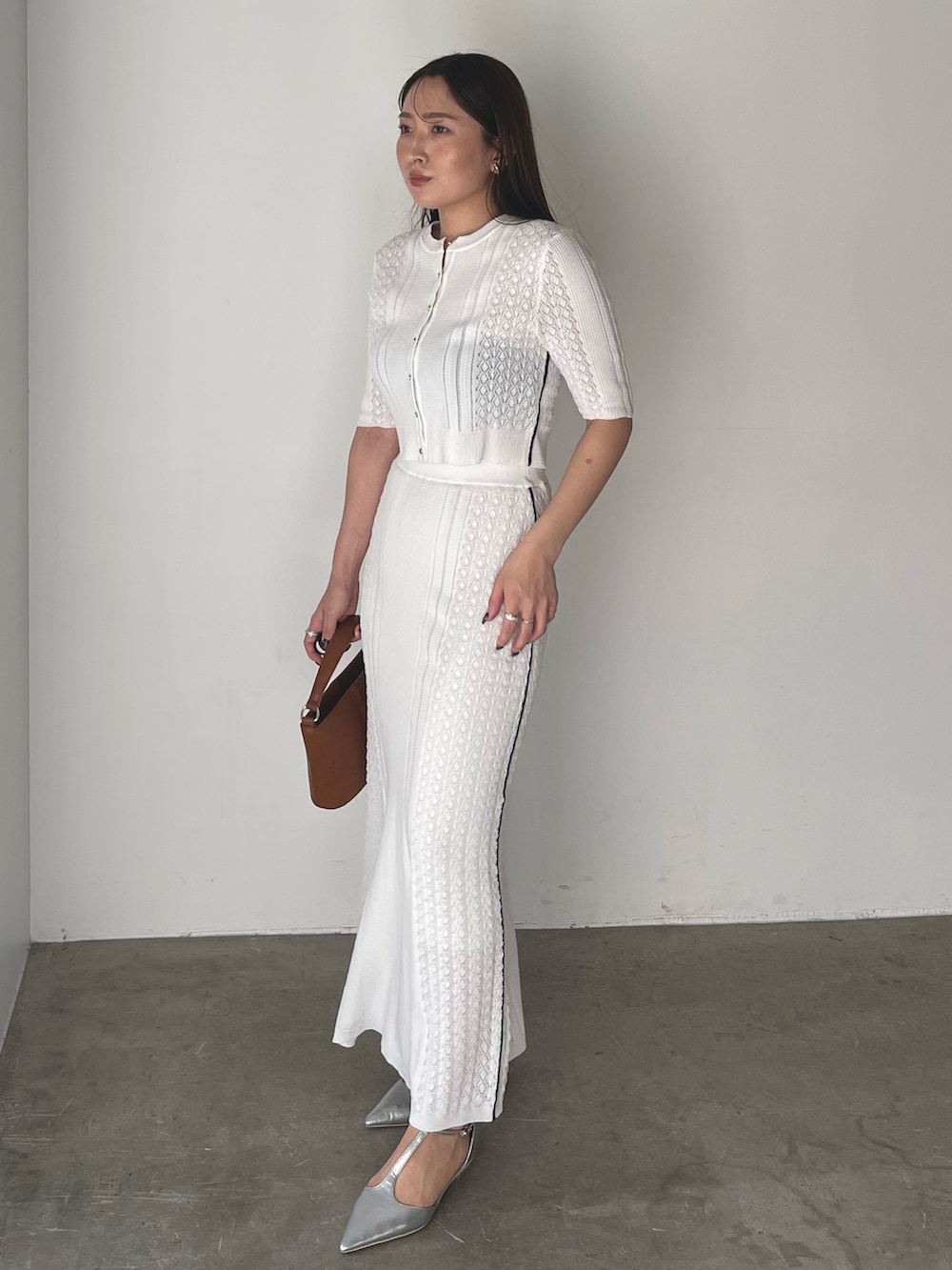 イエロー系のハンドバッグ、シルバー系のパンプス、ホワイト系のワンピースを着用したレディースの冬コーディネートの2枚目の写真