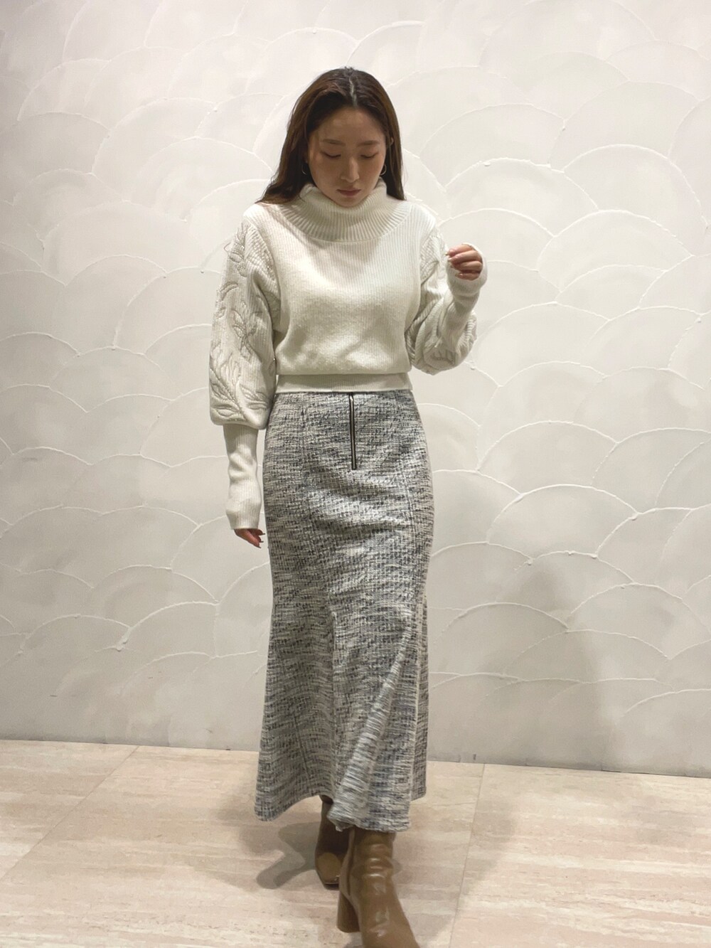 ホワイト系のニット/セーター、ブラック系のスカート、ベージュ系のブーツを着用したレディースの秋コーディネートの2枚目の写真