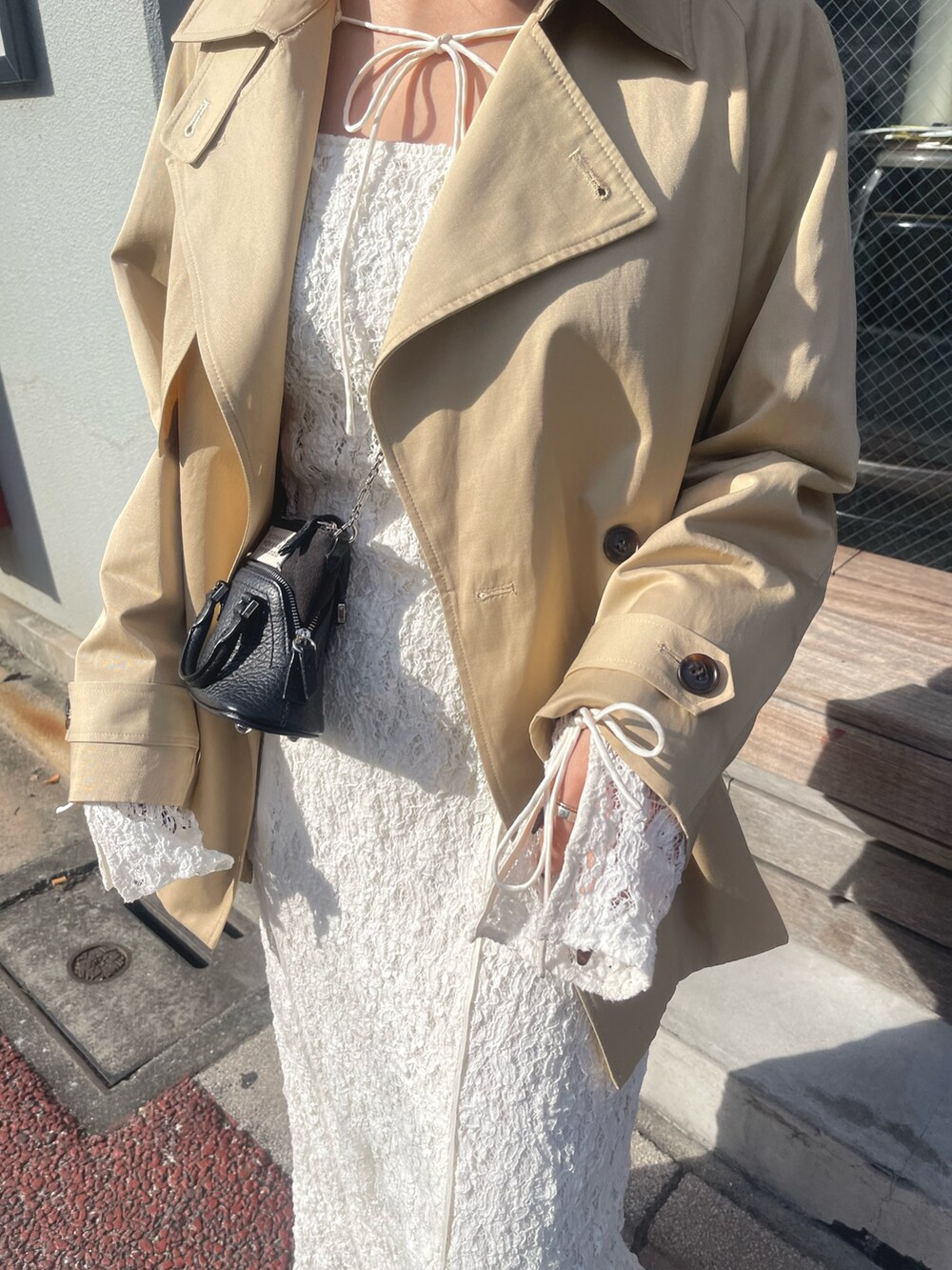 ホワイト系のワンピース、ベージュ系のトレンチコート、ゴールド系のピアス（両耳用）を着用したレディースの冬コーディネートの6枚目の写真