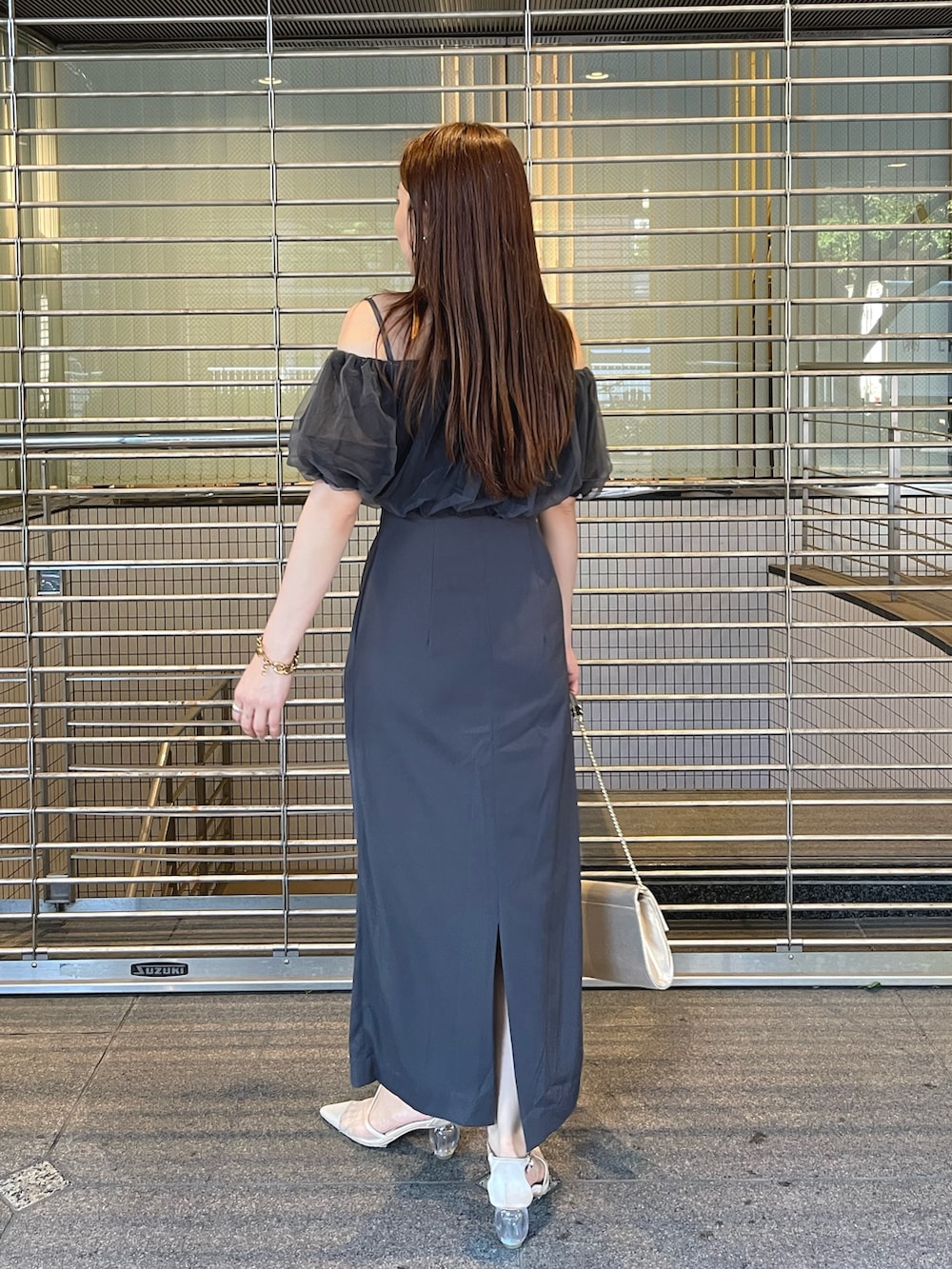 グレー系のドレス、ゴールド系のクラッチバッグ、ゴールド系のピアス（両耳用）を着用したレディースの夏コーディネートの6枚目の写真