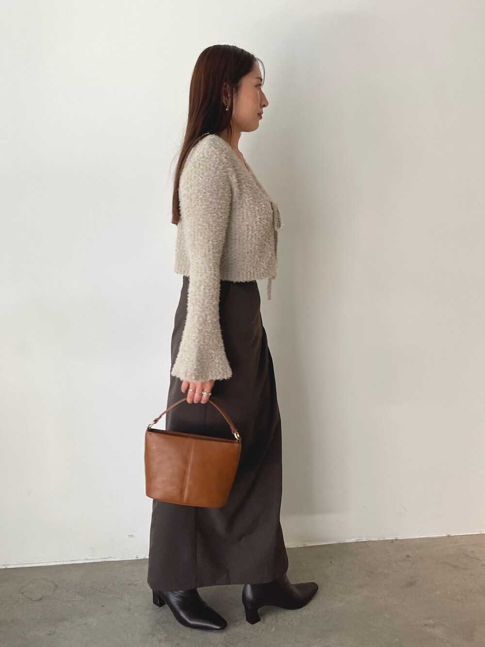 グレー系のアンサンブル、イエロー系のハンドバッグ、ブラウン系のスカートを着用したレディースの秋コーディネートの4枚目の写真