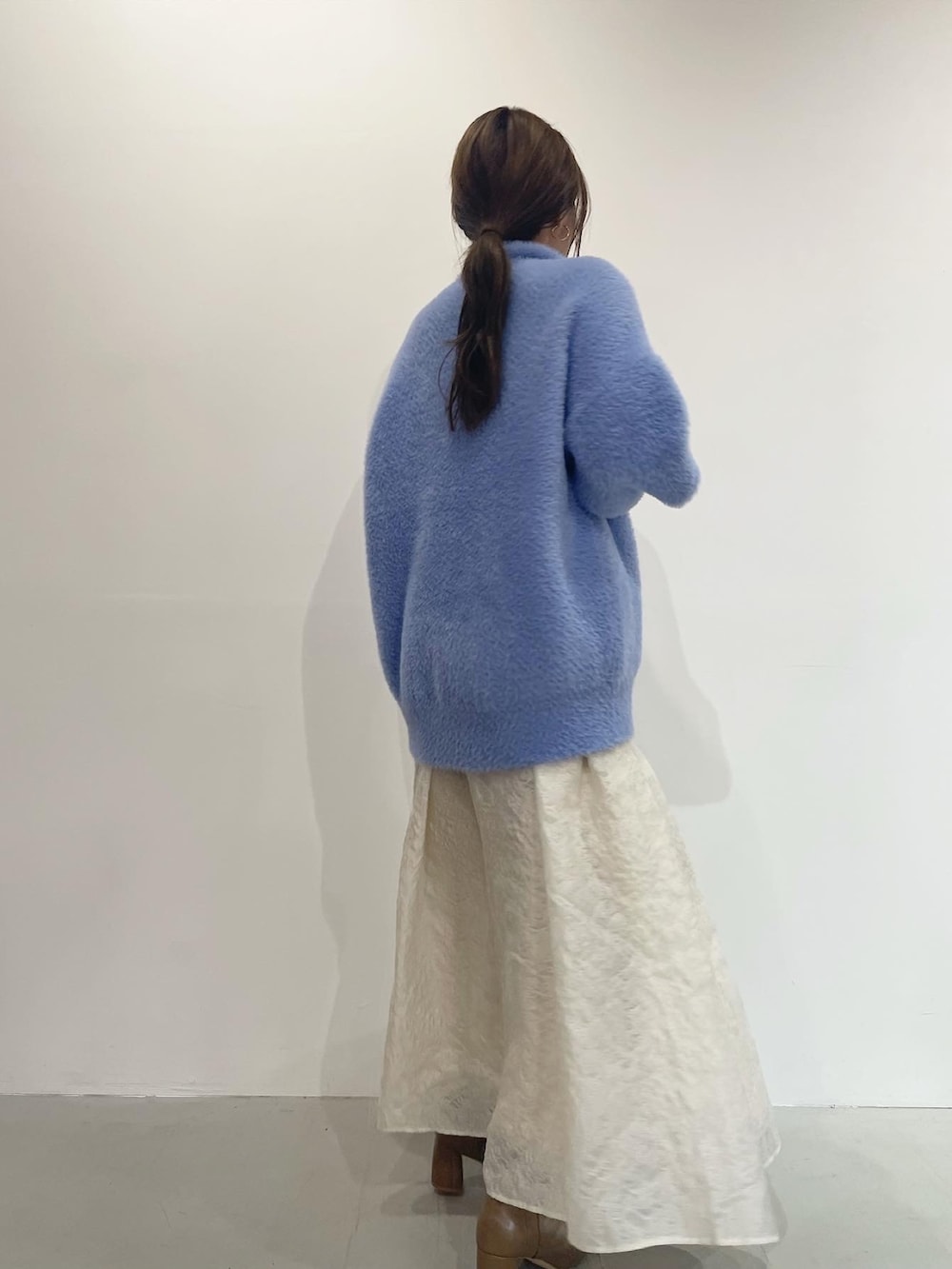 ブルー系のニット/セーター、ベージュ系のブーツ、ホワイト系のスカートを着用したレディースの秋コーディネートの4枚目の写真