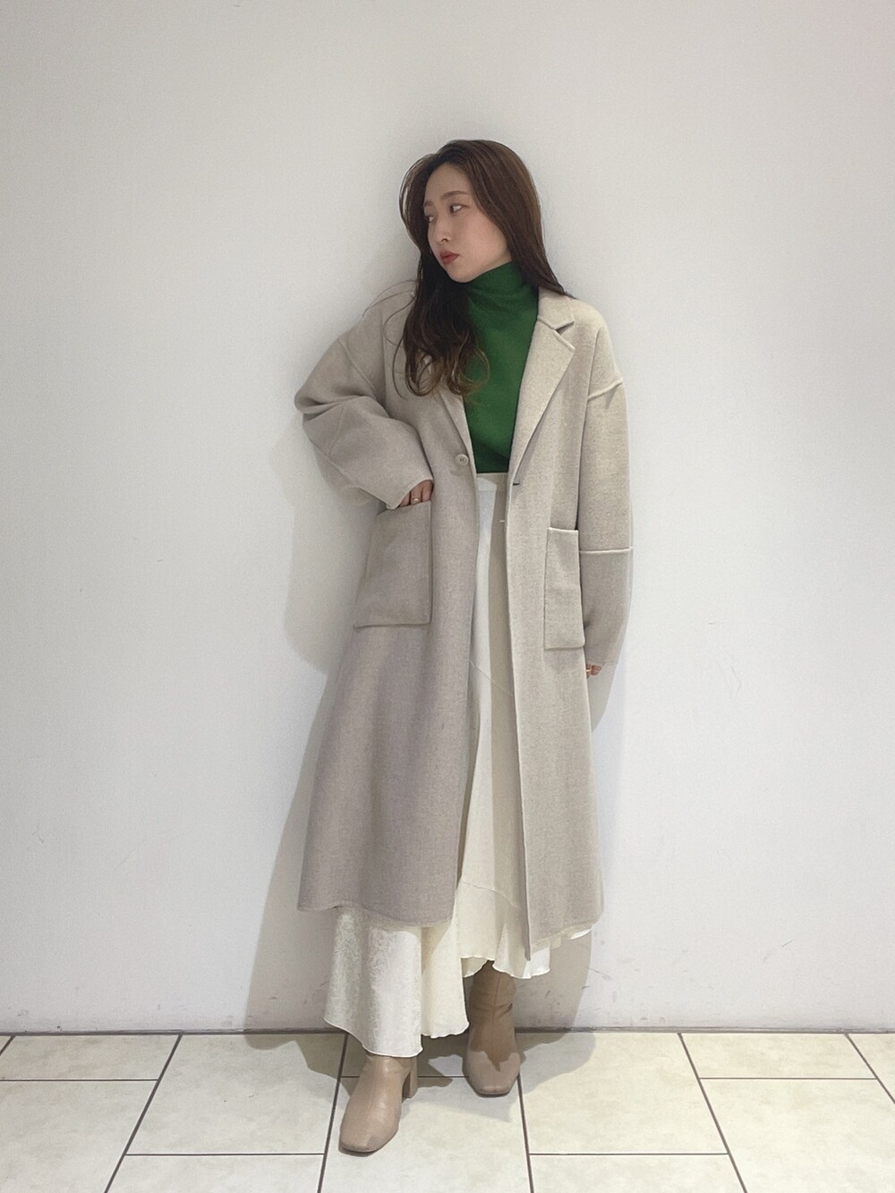 ホワイト系のスカート、ベージュ系のその他アウター、グリーン系のニット/セーターを着用したレディースの冬コーディネートの2枚目の写真