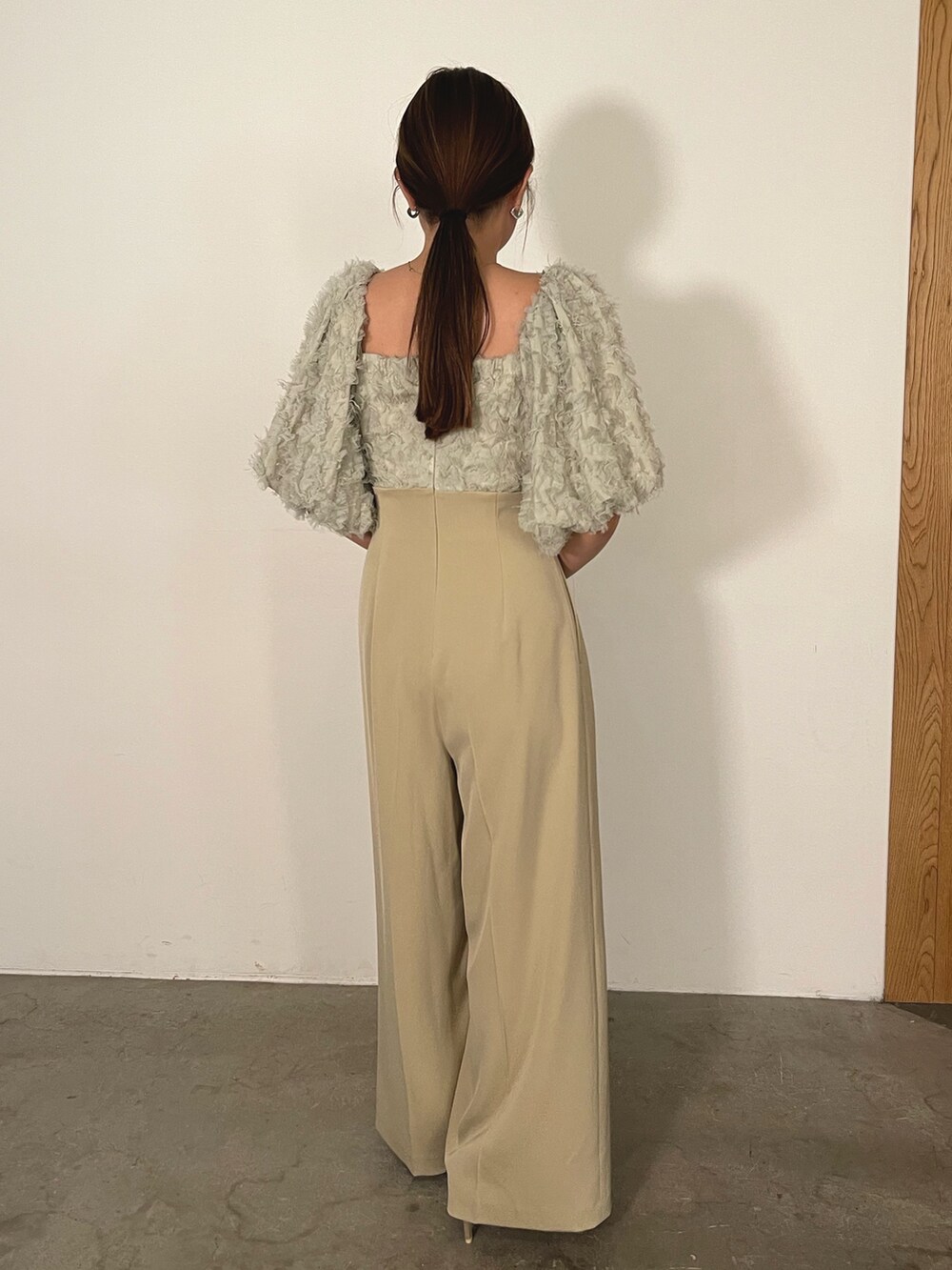 ゴールド系のハンドバッグ、ゴールド系のパンプス、グリーン系のパンツドレスを着用したレディースの冬コーディネートの8枚目の写真