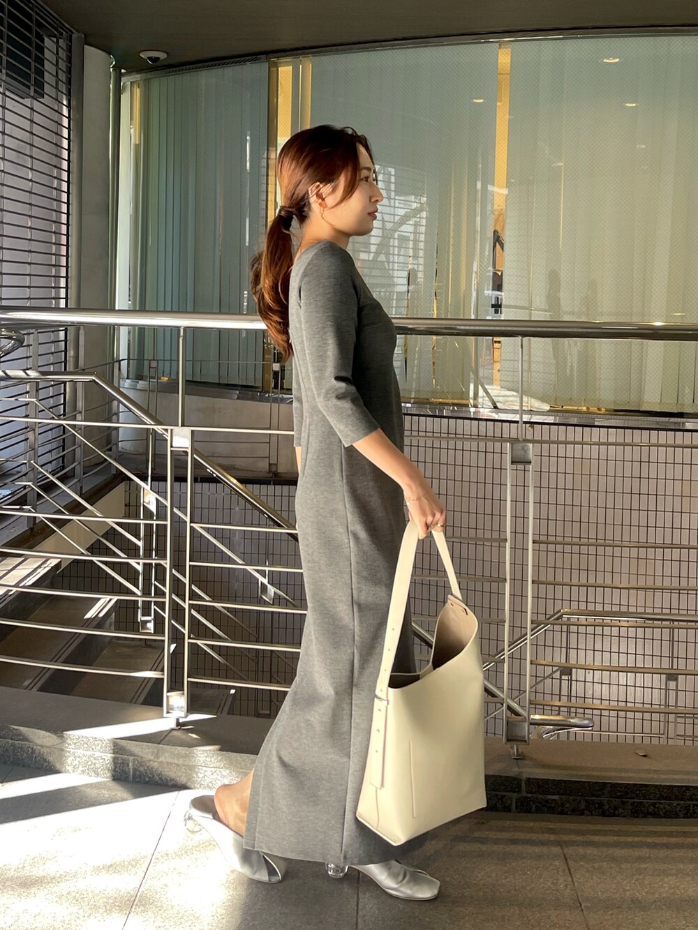 グレー系のワンピース、ホワイト系のショルダーバッグ、シルバー系のパンプスを着用したレディースの冬コーディネートの2枚目の写真