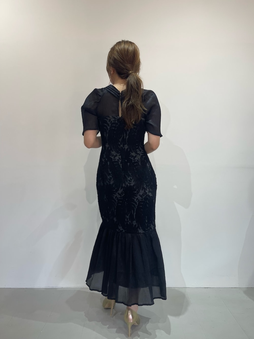 ブラック系のドレス、ゴールド系のパンプス、ゴールド系のピアス（両耳用）を着用したレディースの秋コーディネートの5枚目の写真