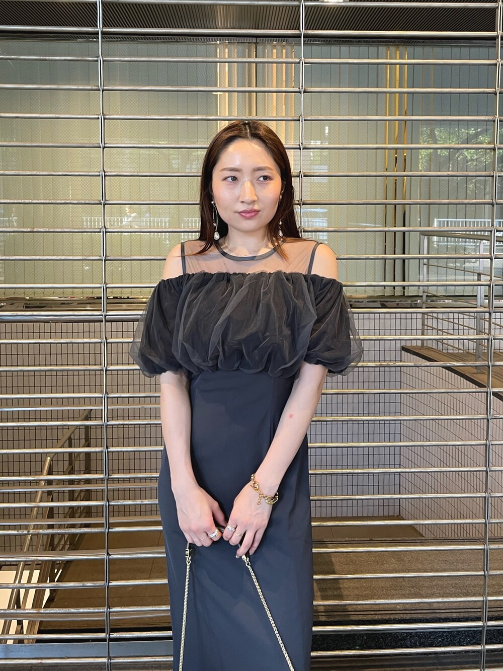 グレー系のドレス、ゴールド系のクラッチバッグ、ゴールド系のピアス（両耳用）を着用したレディースの夏コーディネートの9枚目の写真