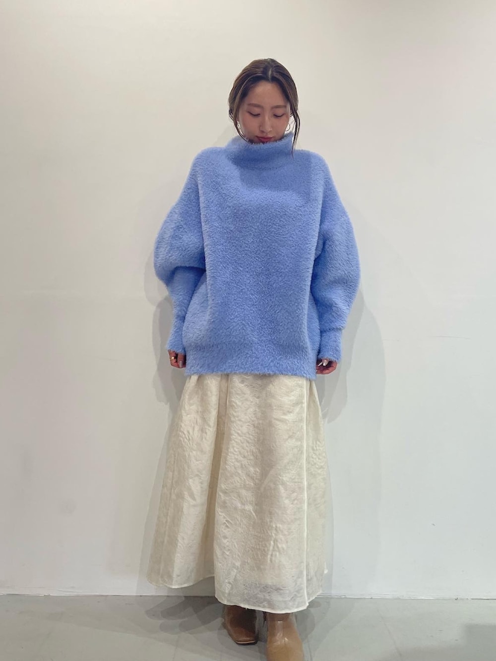 ブルー系のニット/セーター、ベージュ系のブーツ、ホワイト系のスカートを着用したレディースの秋コーディネートの2枚目の写真