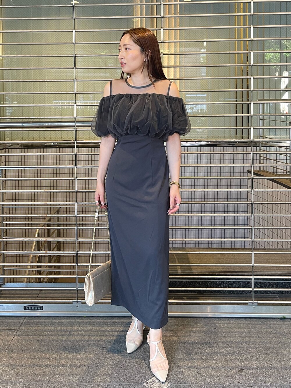 グレー系のドレス、ゴールド系のクラッチバッグ、ゴールド系のピアス（両耳用）を着用したレディースの夏コーディネートの3枚目の写真