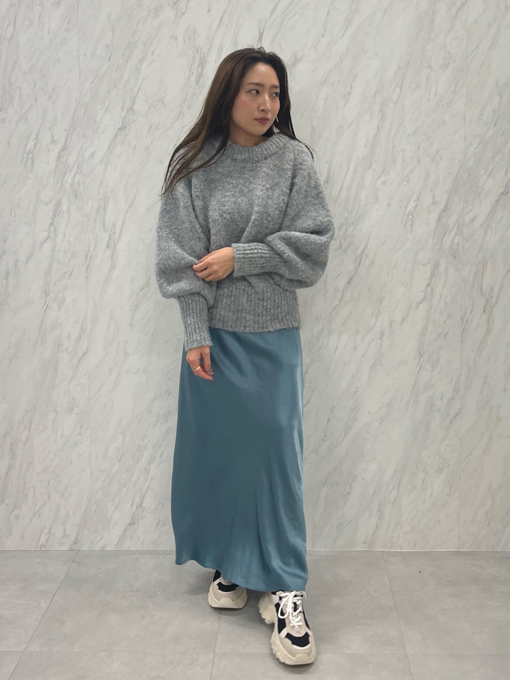 グレー系のニット/セーター、ブルー系のスカート、ブラック系のスニーカーを着用したレディースの冬コーディネートの2枚目の写真