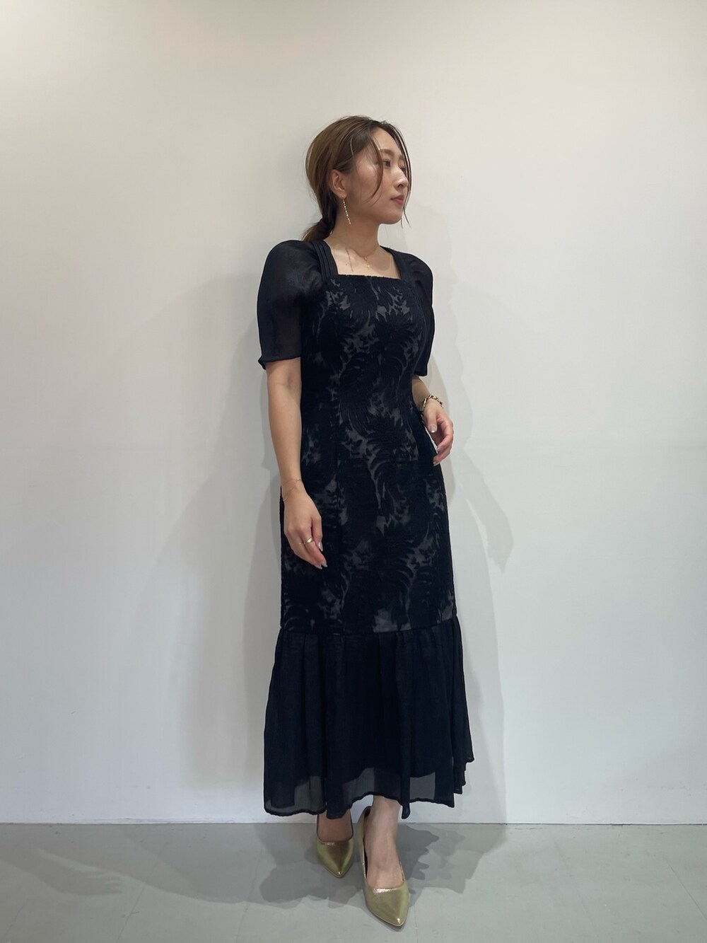 ブラック系のドレス、ゴールド系のパンプス、ゴールド系のピアス（両耳用）を着用したレディースの秋コーディネートの3枚目の写真