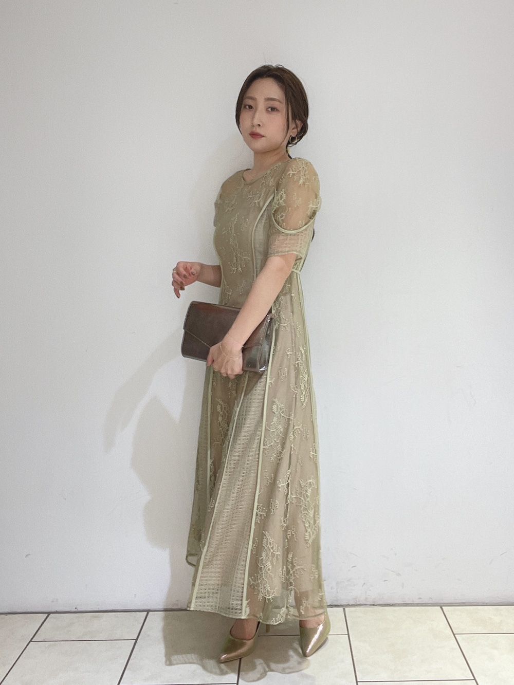 ゴールド系のハンドバッグ、グリーン系のドレス、ゴールド系のパンプスを着用したレディースの冬コーディネートの5枚目の写真