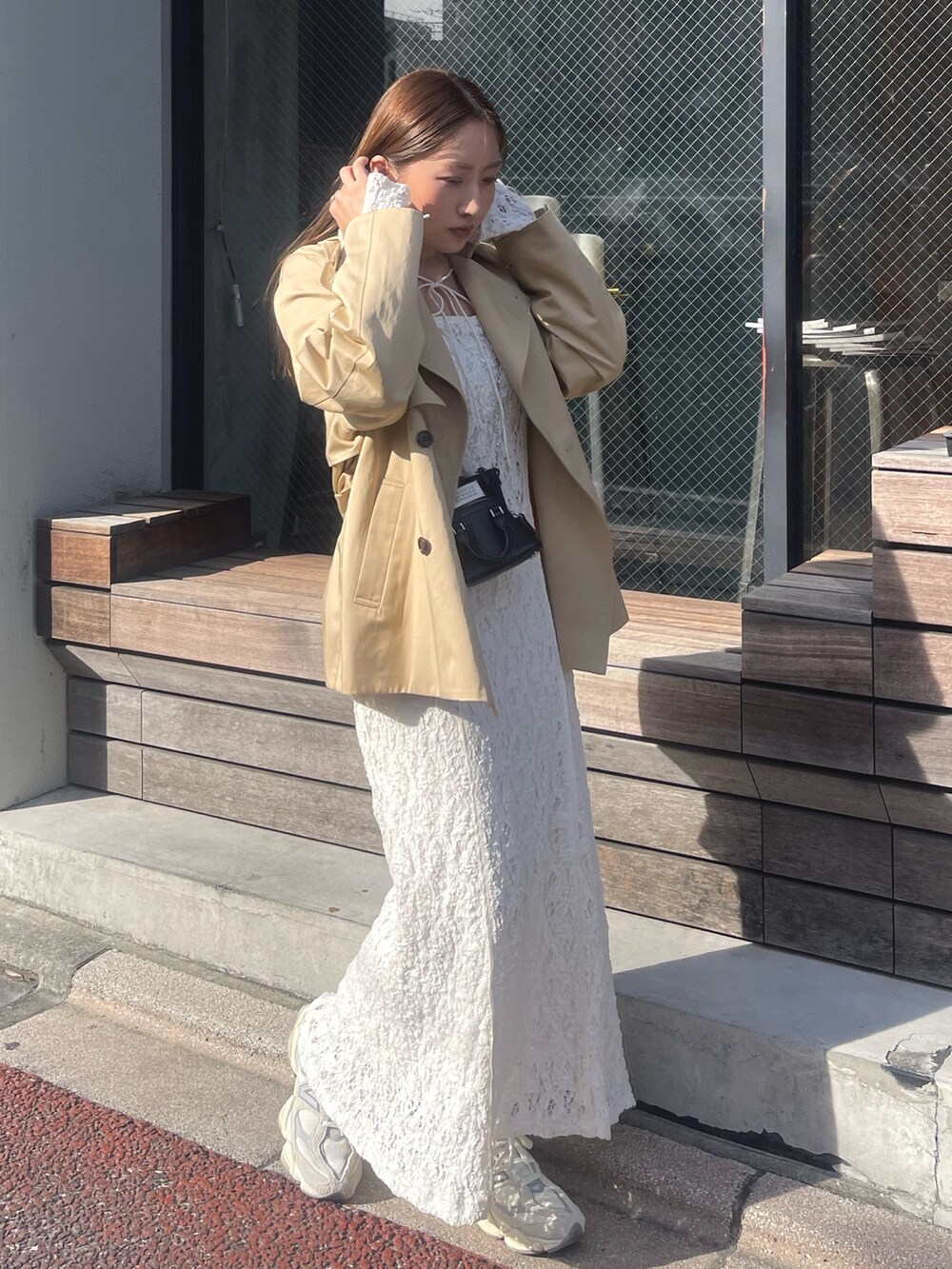 ホワイト系のワンピース、ベージュ系のトレンチコート、ゴールド系のピアス（両耳用）を着用したレディースの冬コーディネートの4枚目の写真