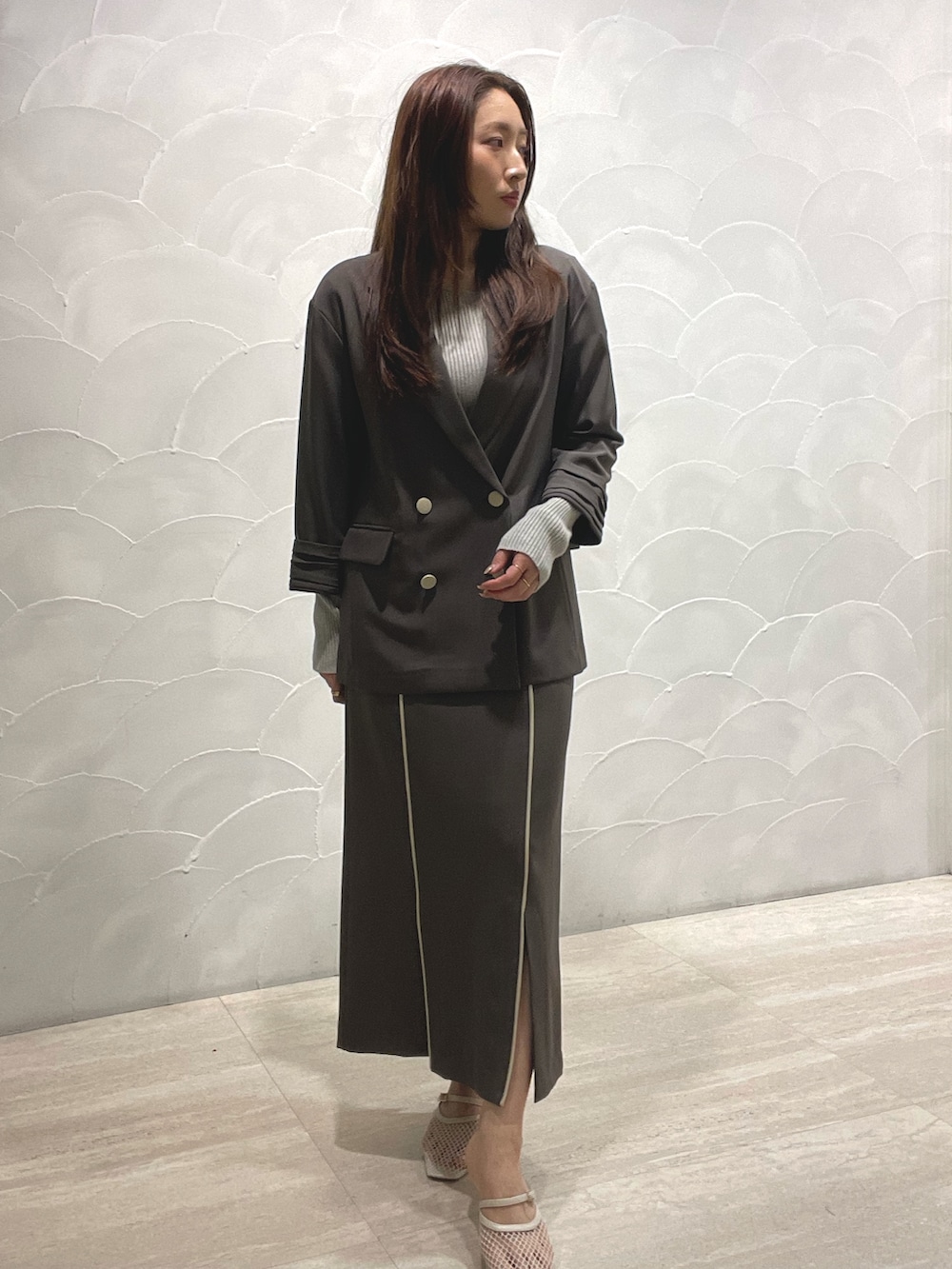 グレー系のスカート、ホワイト系のサンダル、グレー系のニット/セーターを着用したレディースの春コーディネートの2枚目の写真