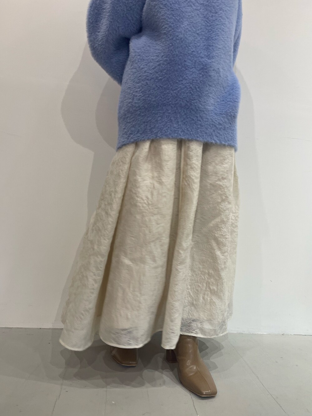 ブルー系のニット/セーター、ベージュ系のブーツ、ホワイト系のスカートを着用したレディースの秋コーディネートの5枚目の写真