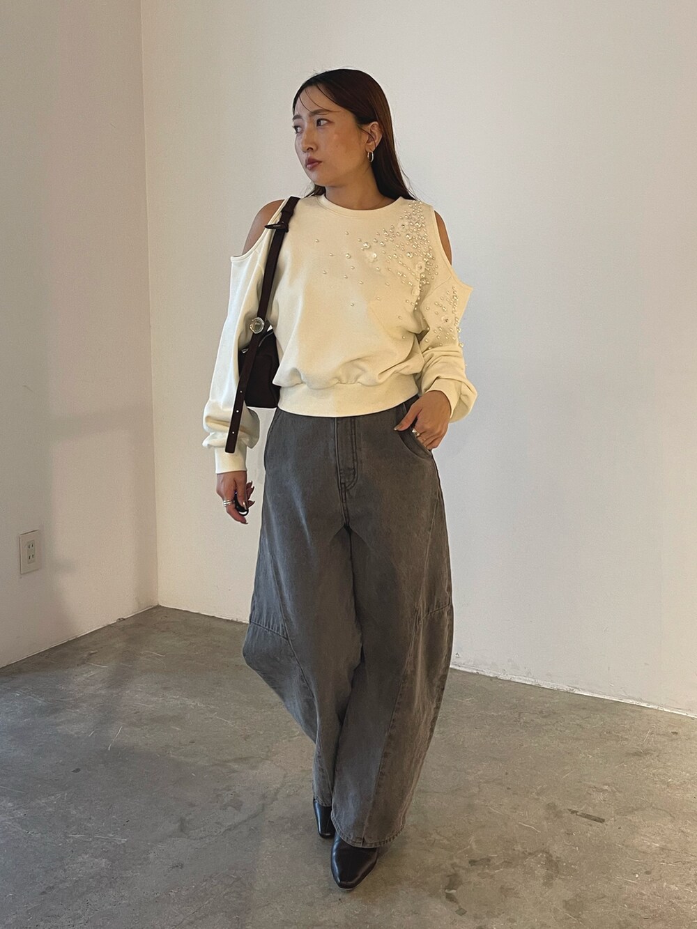 グレー系のデニムパンツ、ブラック系のブーツ、ブラウン系のハンドバッグを着用したレディースの秋コーディネートの2枚目の写真
