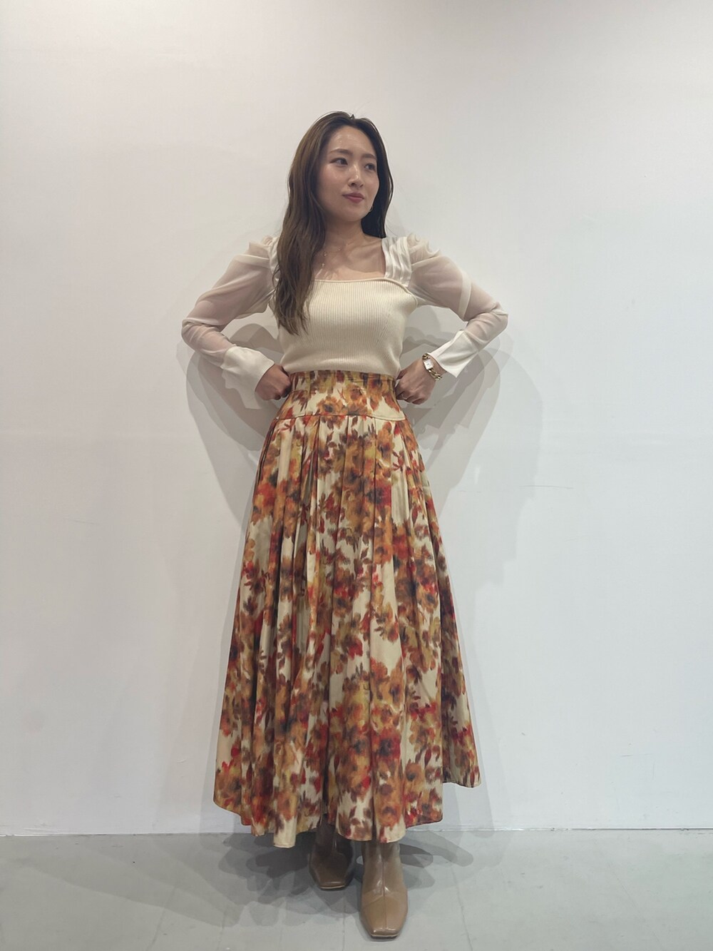 ベージュ系のブーツ、オレンジ系のスカート、ホワイト系のニット/セーターを着用したレディースの秋コーディネートの2枚目の写真