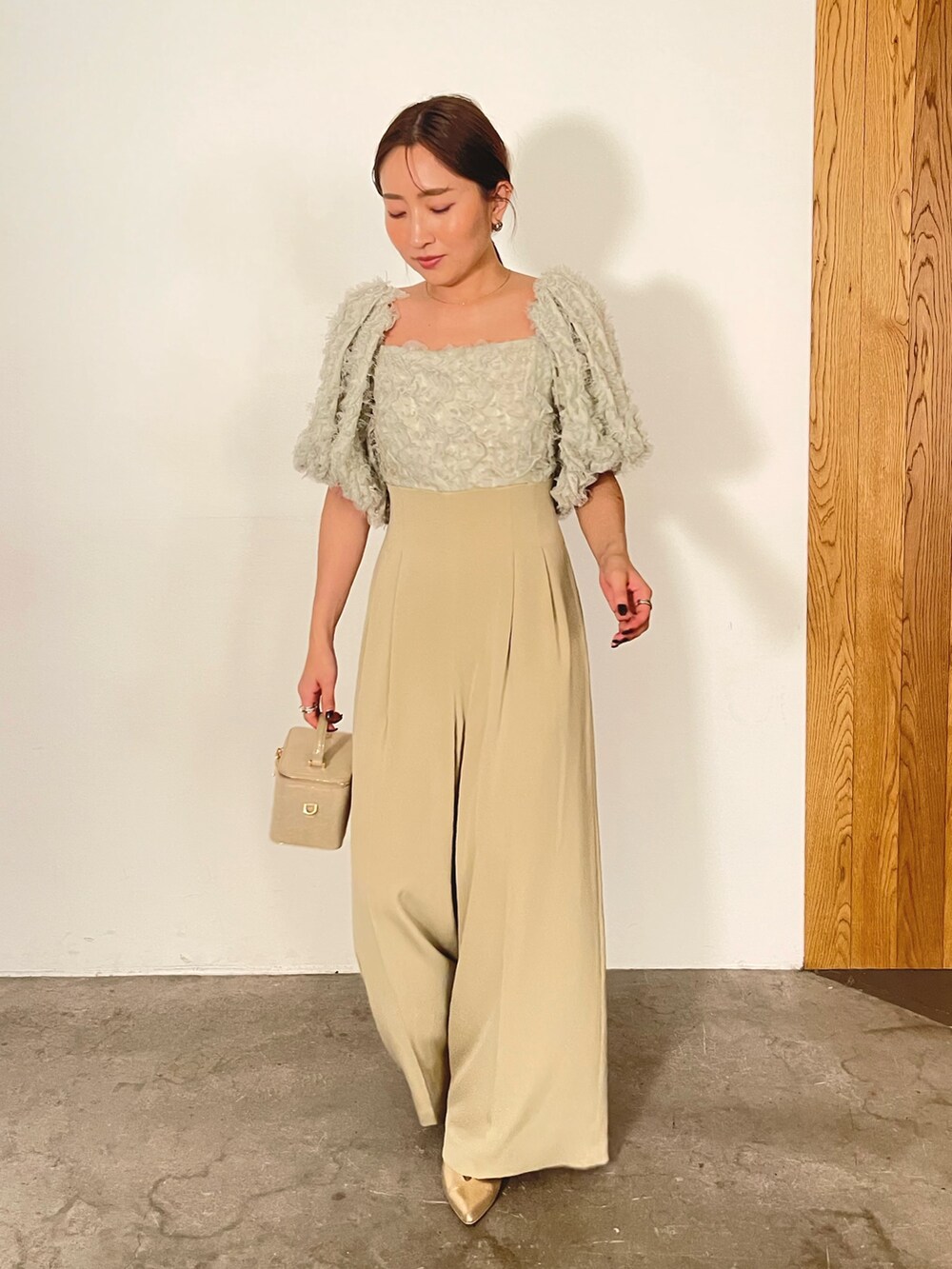 ゴールド系のハンドバッグ、ゴールド系のパンプス、グリーン系のパンツドレスを着用したレディースの冬コーディネートの2枚目の写真