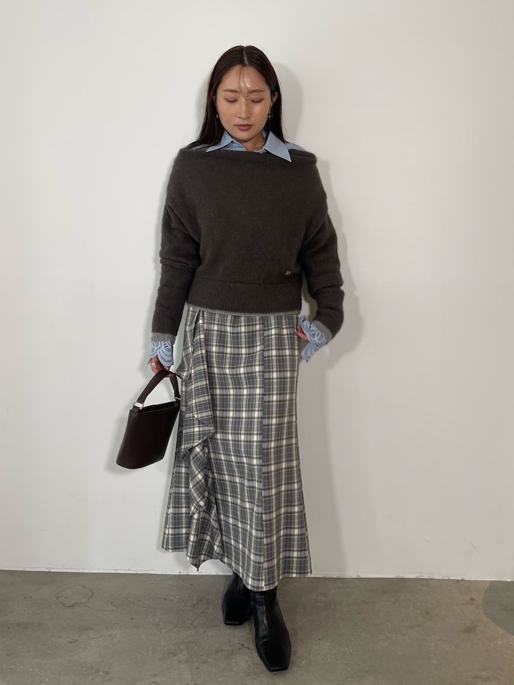 グレー系のスカート、ブラック系のブーツ、ブラウン系のハンドバッグを着用したレディースの秋コーディネートの3枚目の写真