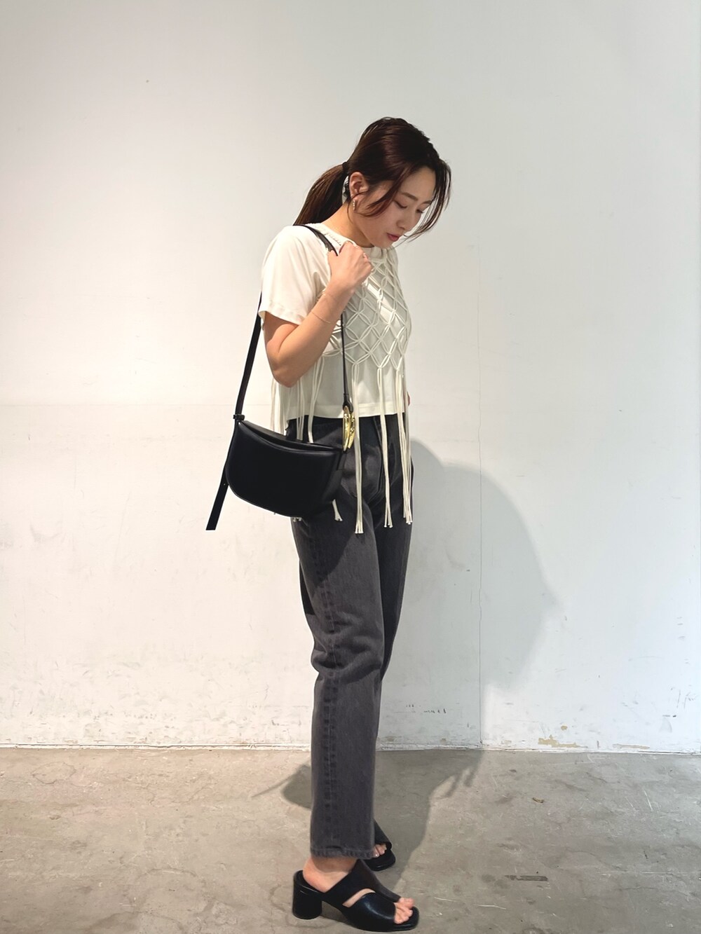 ブラック系のデニムパンツ、ブラック系のサンダル、ブラック系のショルダーバッグを着用したレディースの春コーディネートの3枚目の写真