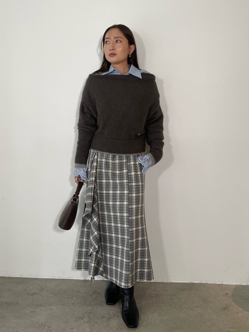 グレー系のスカート、ブラック系のブーツ、ブラウン系のハンドバッグを着用したレディースの秋コーディネートの2枚目の写真