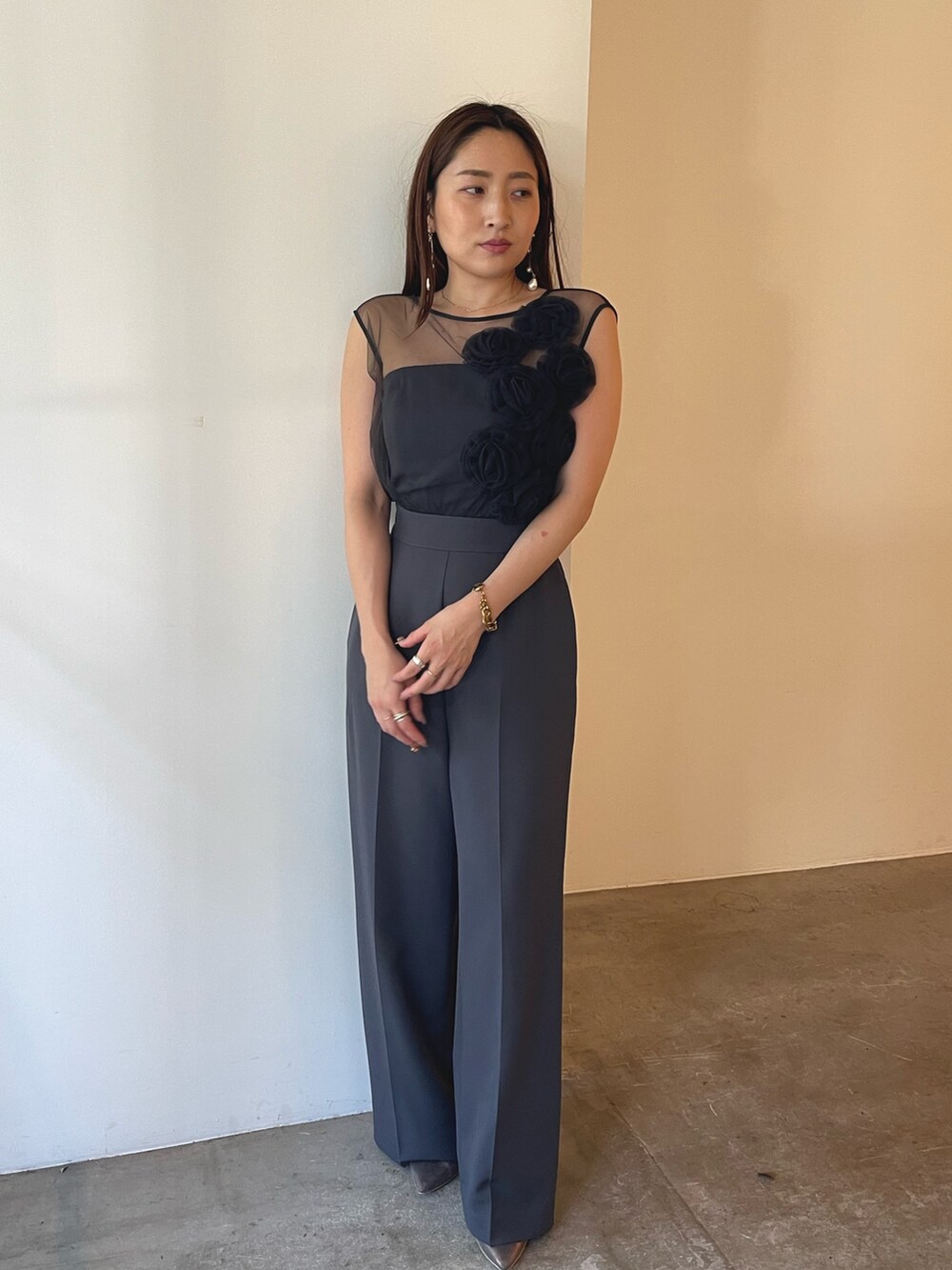 シルバー系のパンプス、グレー系のパンツドレス、ゴールド系のピアス（両耳用）を着用したレディースの夏コーディネートの2枚目の写真