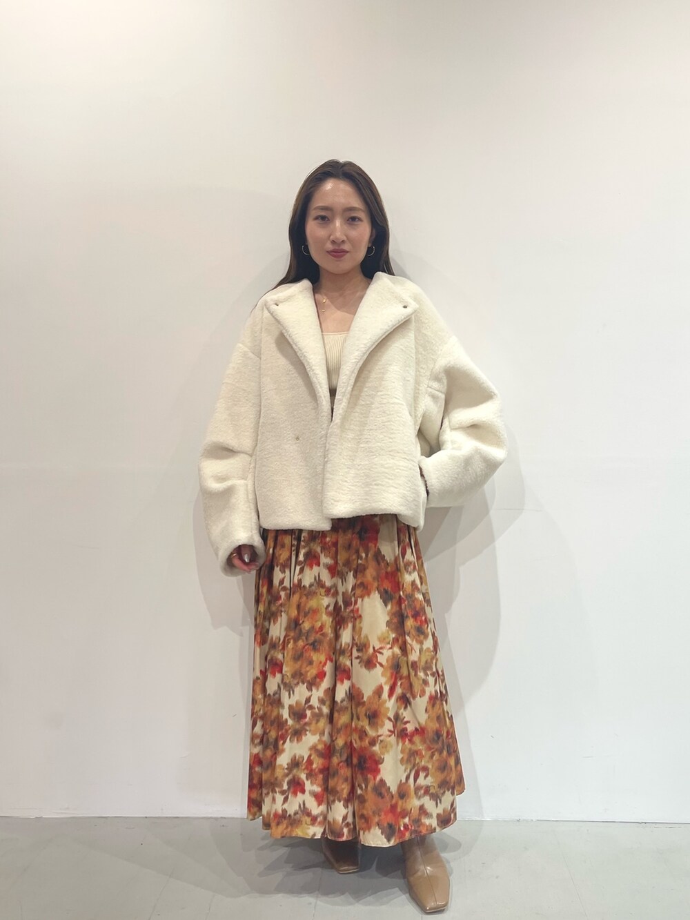 オレンジ系のスカート、ベージュ系のブーツ、ホワイト系のニット/セーターを着用したレディースの秋コーディネートの5枚目の写真