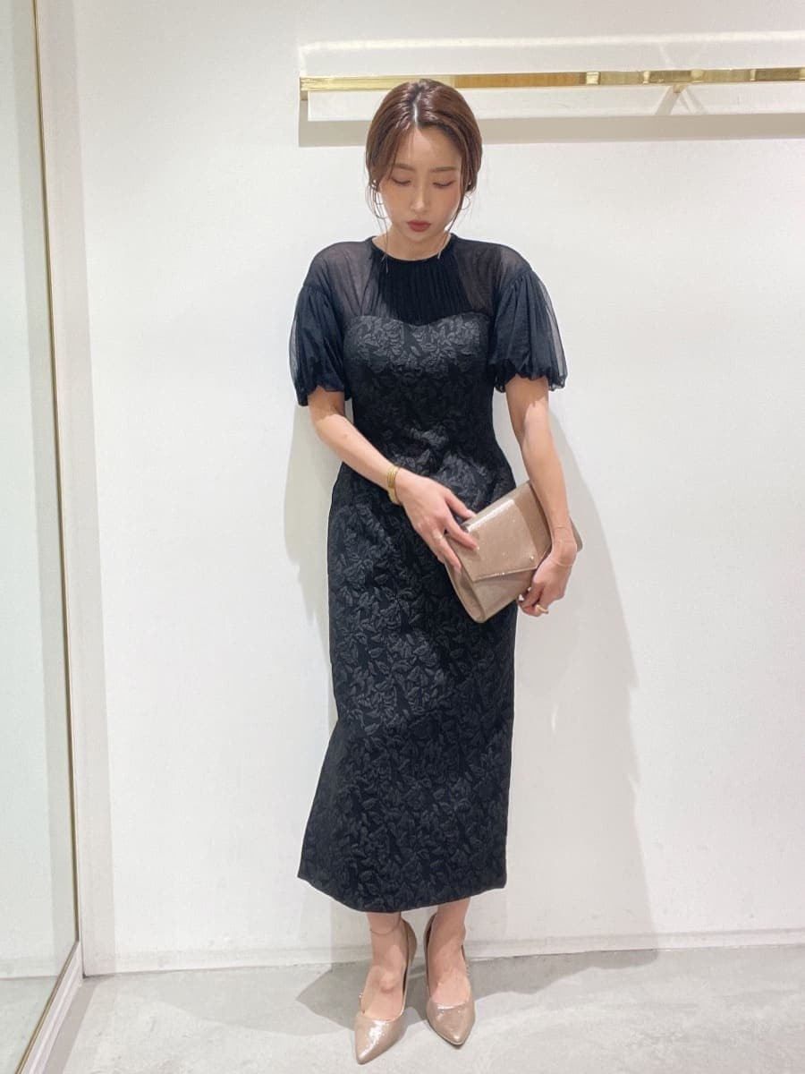 ゴールド系のクラッチバッグ、ゴールド系のパンプス、ブラック系のドレスを着用したレディースの秋コーディネートの2枚目の写真
