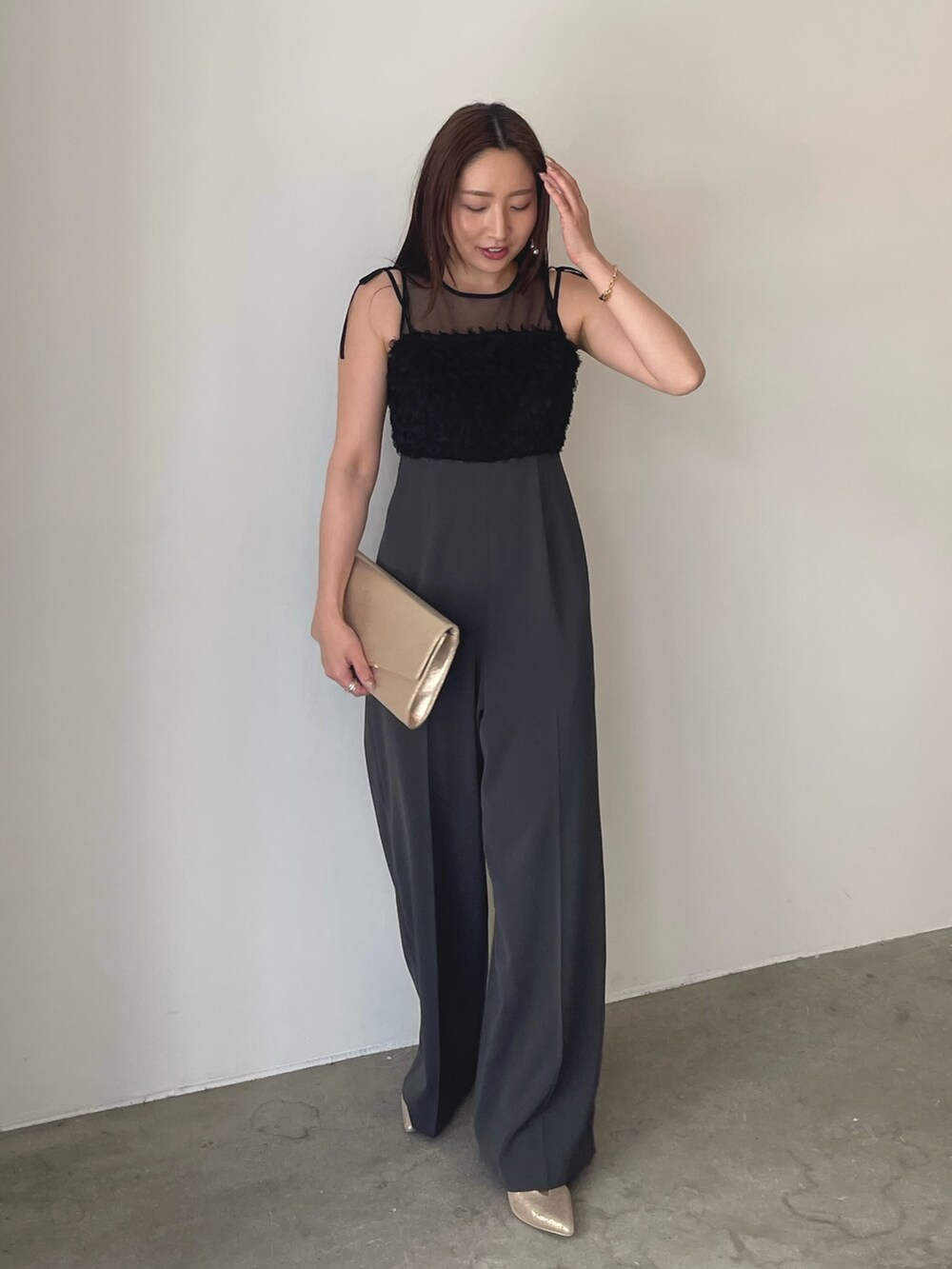 グレー系のパンツドレス、ゴールド系のパンプス、ゴールド系のクラッチバッグを着用したレディースの春コーディネートの4枚目の写真