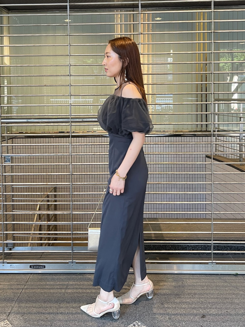 グレー系のドレス、ゴールド系のクラッチバッグ、ゴールド系のピアス（両耳用）を着用したレディースの夏コーディネートの5枚目の写真