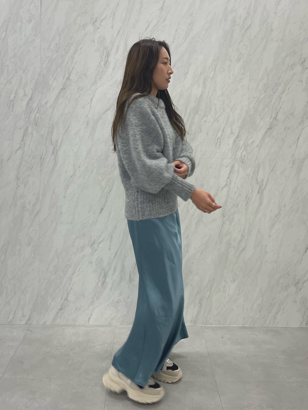 グレー系のニット/セーター、ブルー系のスカート、ブラック系のスニーカーを着用したレディースの冬コーディネートの3枚目の写真