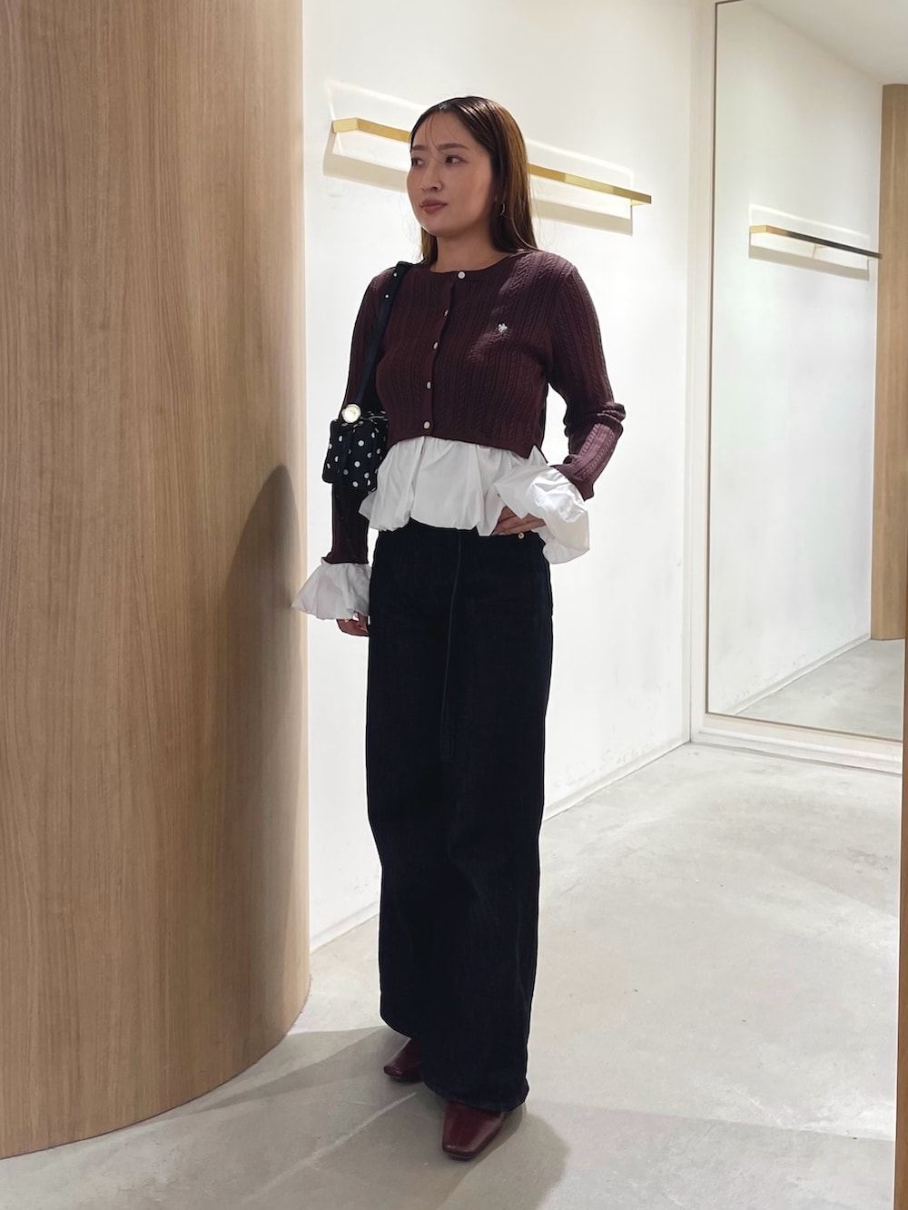 レッド系のブーツ、ブラック系のデニムパンツ、ブラック系のハンドバッグを着用したレディースの秋コーディネートの2枚目の写真