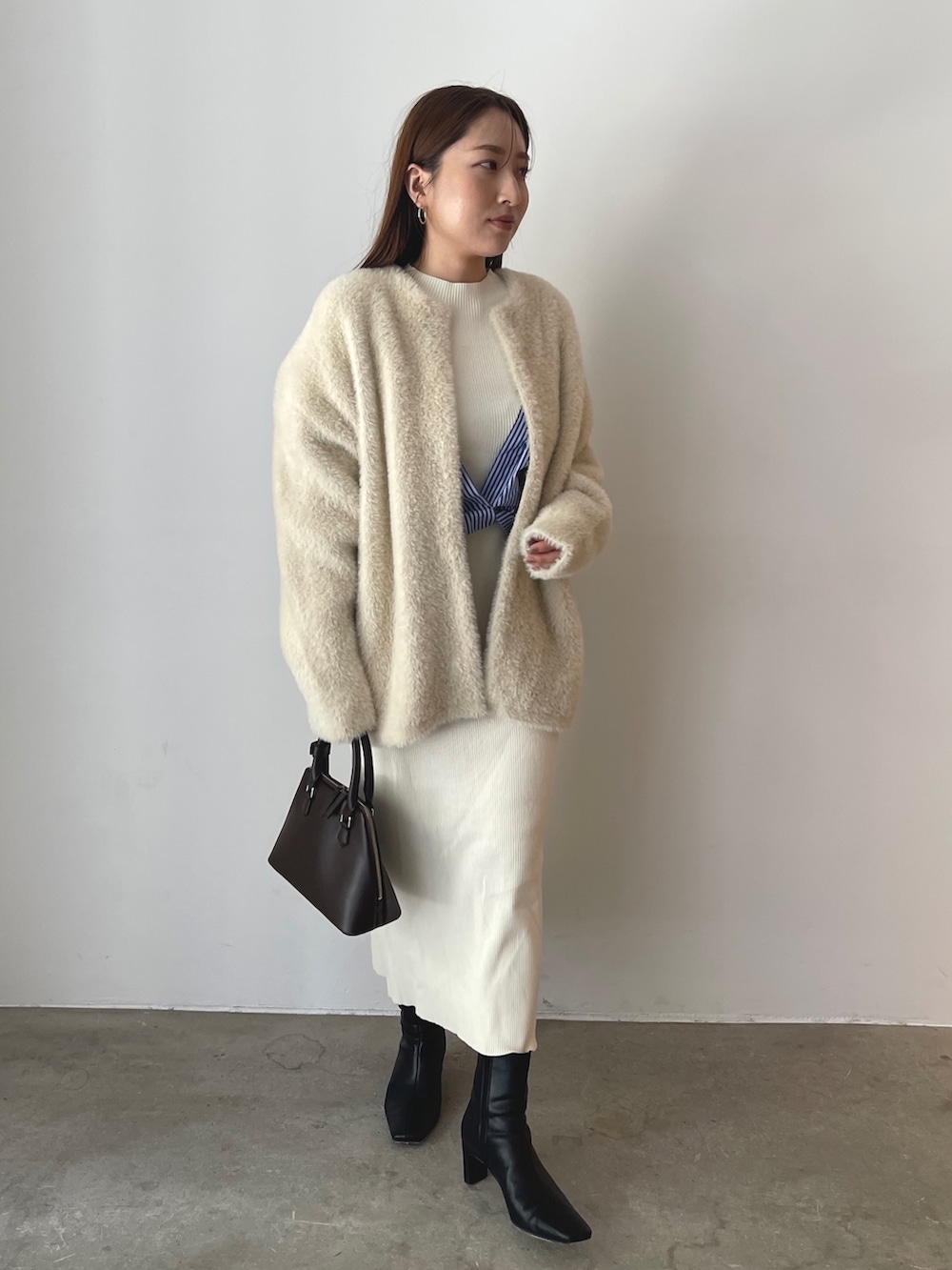 ブラウン系のボストンバッグ、ブラック系のブーツ、ホワイト系のワンピースを着用したレディースの秋コーディネートの4枚目の写真