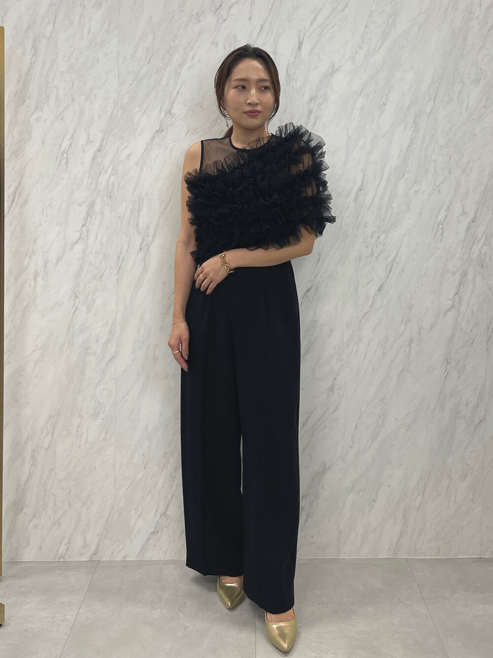 ブラック系のパンツドレス、ゴールド系のパンプスを着用したレディースの冬コーディネートの2枚目の写真