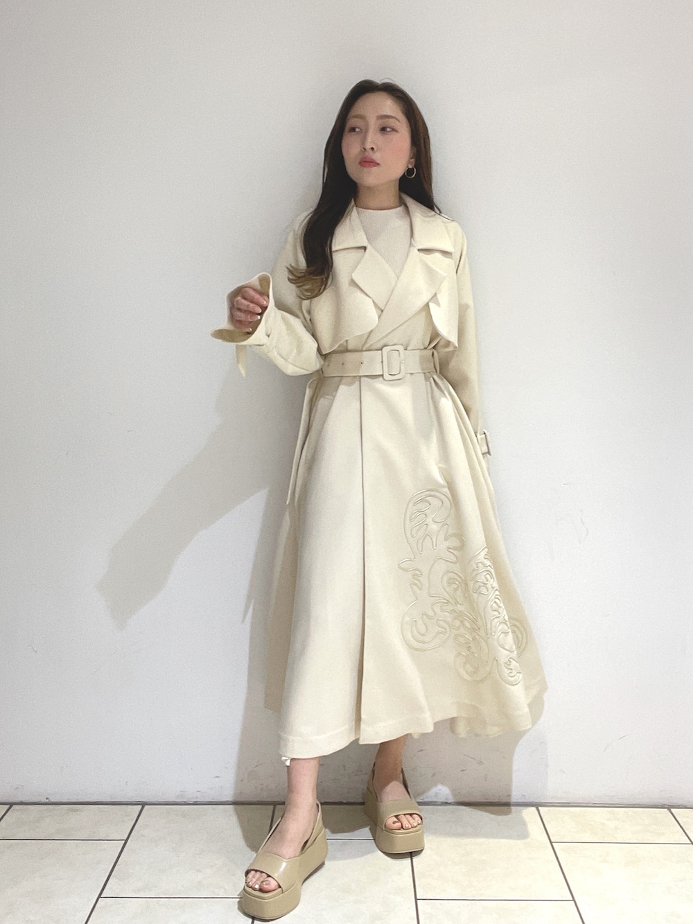 ホワイト系のトレンチコート、ベージュ系のサンダル、グリーン系のショルダーバッグを着用したレディースの冬コーディネートの3枚目の写真