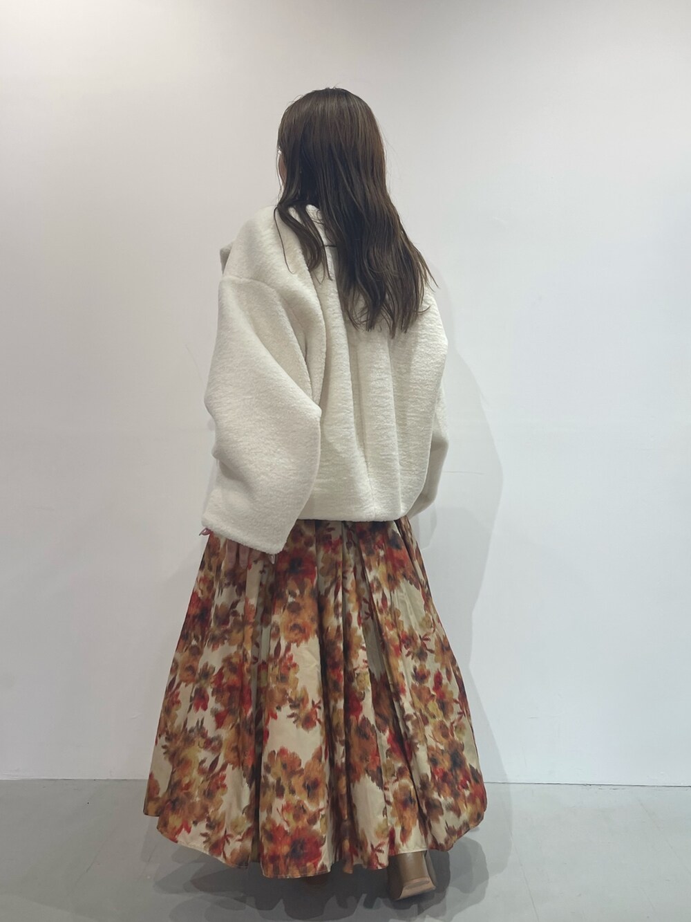 オレンジ系のスカート、ベージュ系のブーツ、ホワイト系のニット/セーターを着用したレディースの秋コーディネートの3枚目の写真