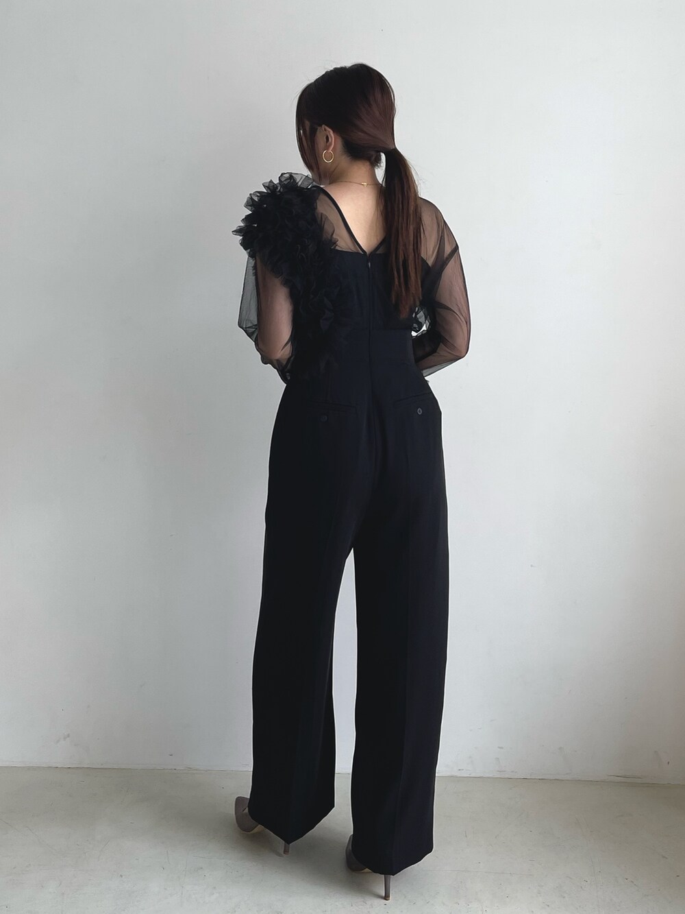 ブラック系のパンツドレス、シルバー系のパンプスを着用したレディースの秋コーディネートの3枚目の写真