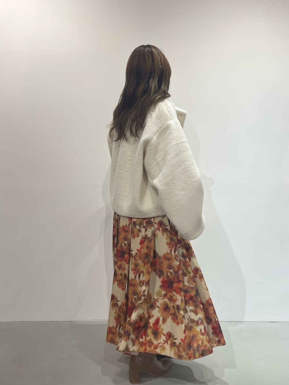 オレンジ系のスカート、ベージュ系のブーツ、ホワイト系のニット/セーターを着用したレディースの秋コーディネートの4枚目の写真