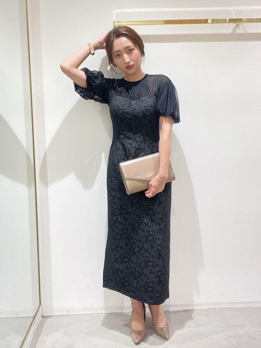 ゴールド系のクラッチバッグ、ゴールド系のパンプス、ブラック系のドレスを着用したレディースの秋コーディネートの3枚目の写真