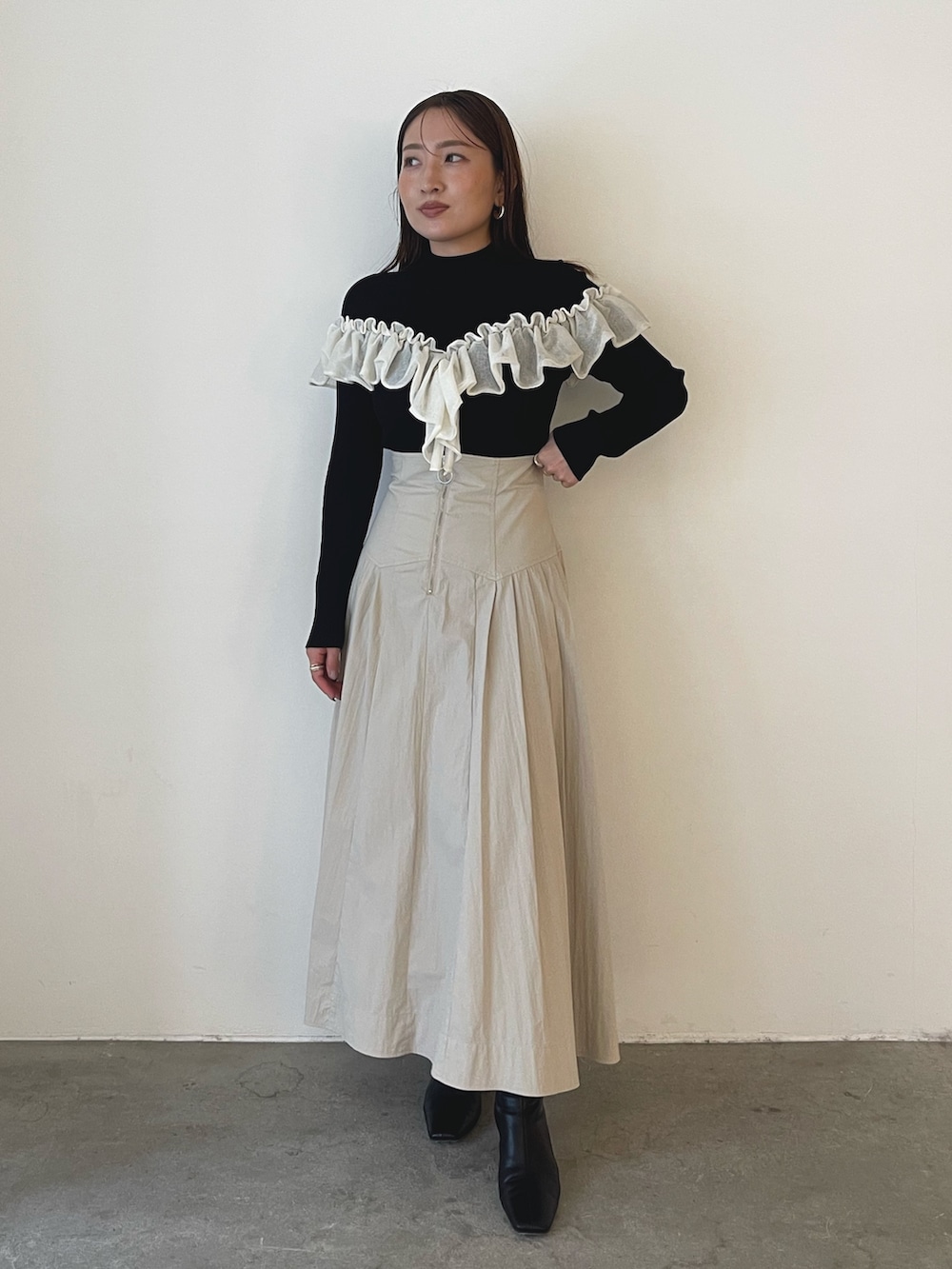 ブラック系のブーツ、ホワイト系のスカート、ブラック系のニット/セーターを着用したレディースの秋コーディネートの2枚目の写真