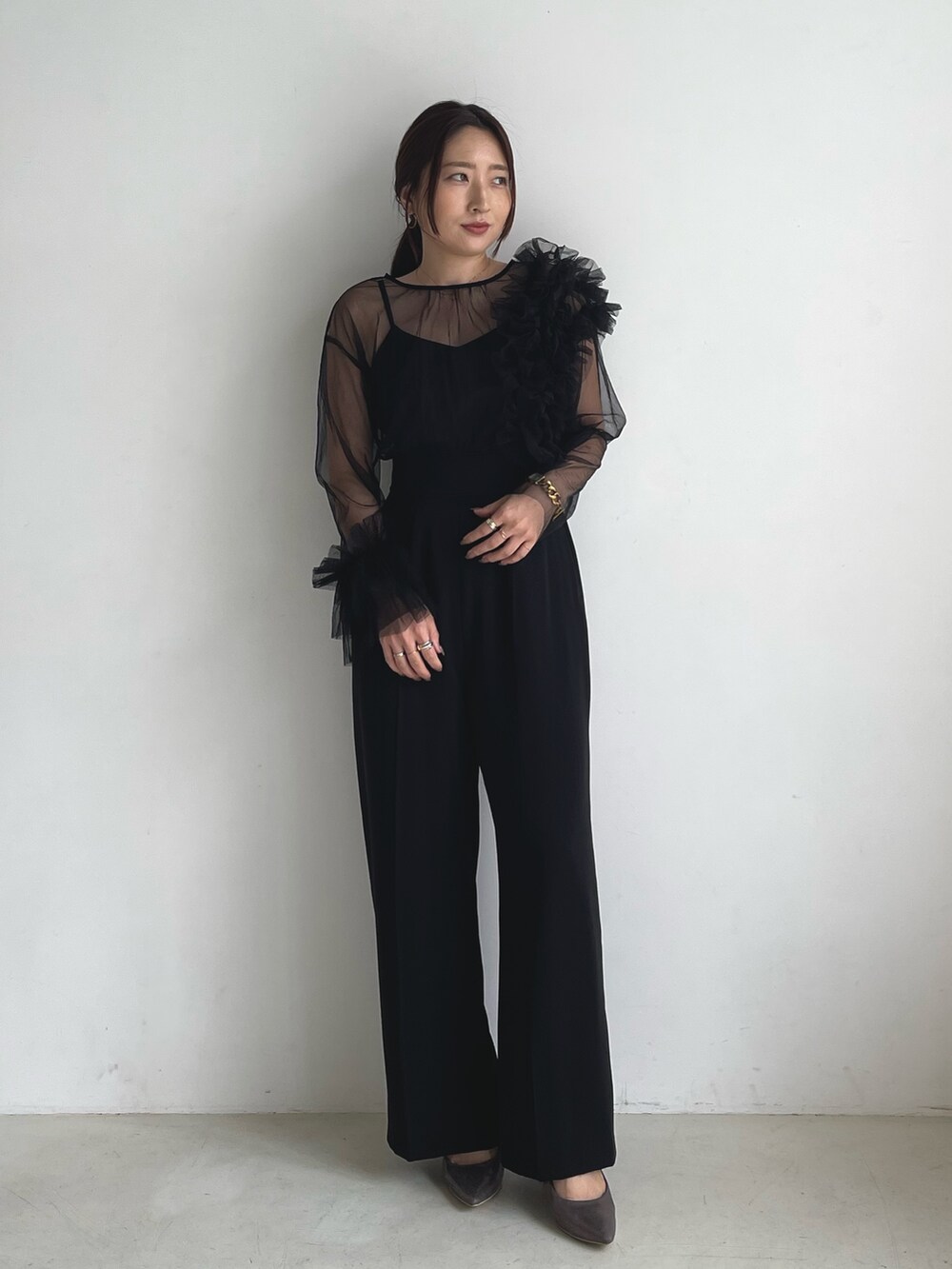 ブラック系のパンツドレス、シルバー系のパンプスを着用したレディースの秋コーディネートの2枚目の写真