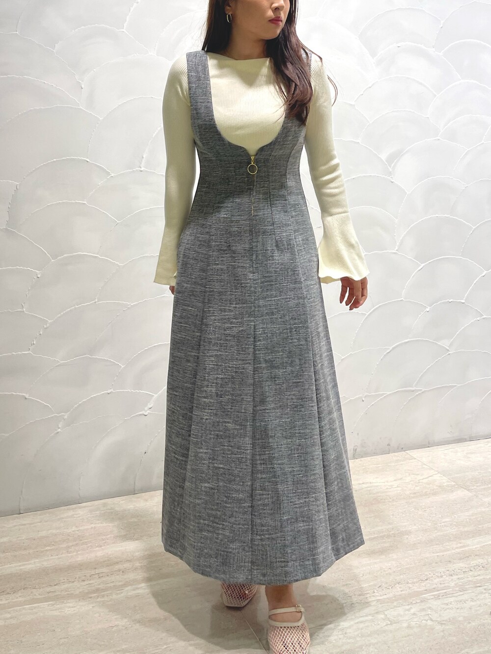 ホワイト系のサンダル、ホワイト系のニット/セーター、グレー系のジャンパースカートを着用したレディースの春コーディネートの2枚目の写真