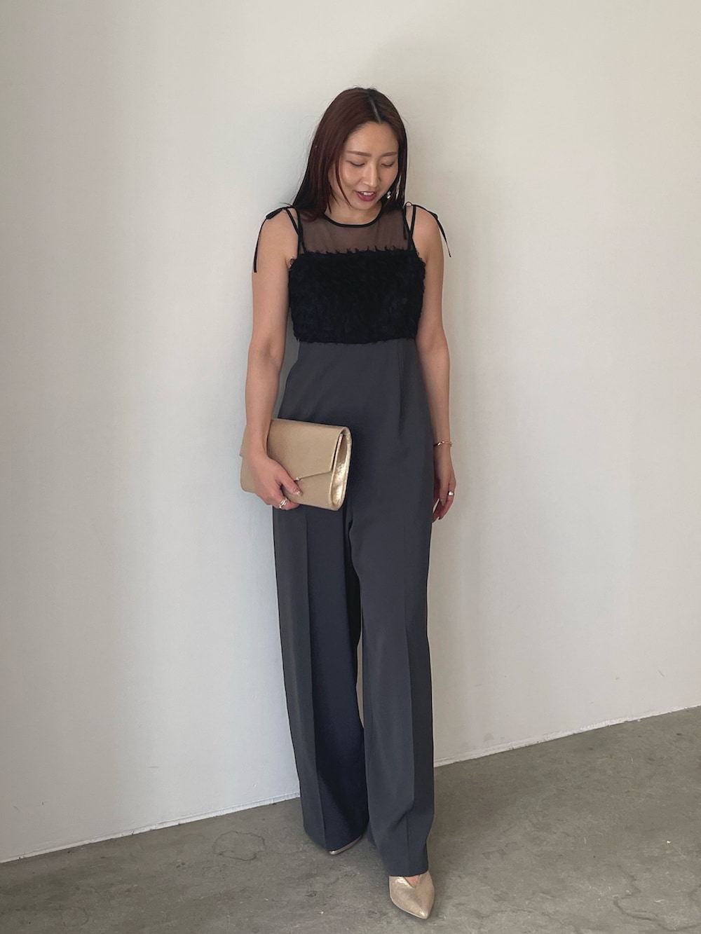 グレー系のパンツドレス、ゴールド系のパンプス、ゴールド系のクラッチバッグを着用したレディースの春コーディネートの2枚目の写真