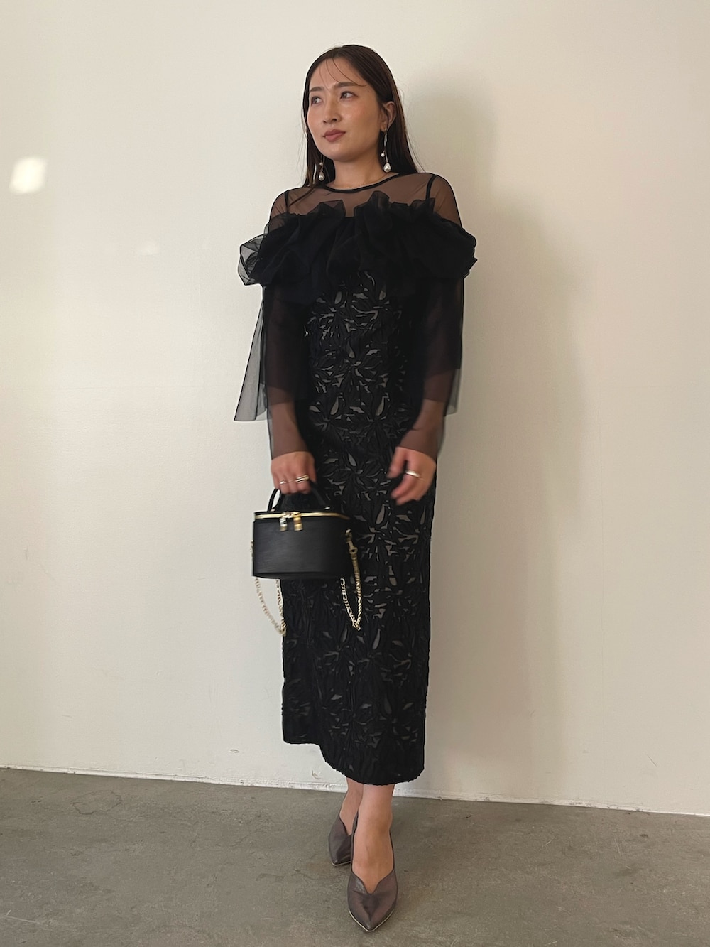 シルバー系のパンプス、ブラック系のハンドバッグ、ブラック系のドレスを着用したレディースの秋コーディネートの2枚目の写真