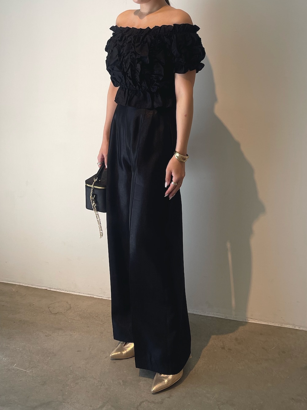 ブラック系のハンドバッグ、ゴールド系のパンプス、ブラック系のパンツドレスを着用したレディースの春コーディネートの4枚目の写真