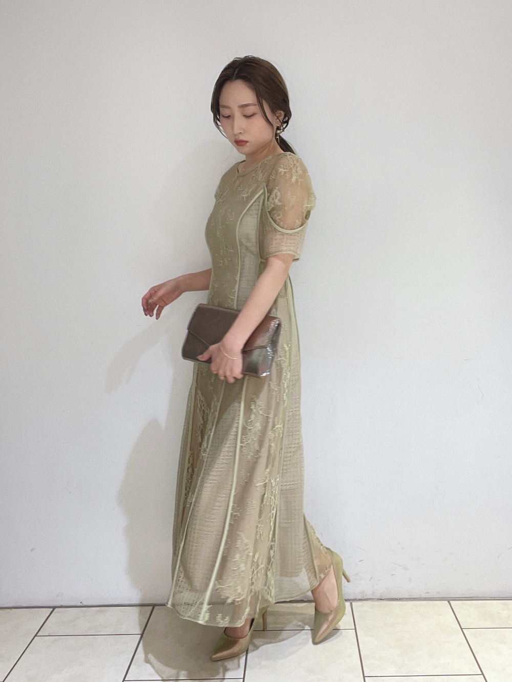 ゴールド系のハンドバッグ、グリーン系のドレス、ゴールド系のパンプスを着用したレディースの冬コーディネートの2枚目の写真