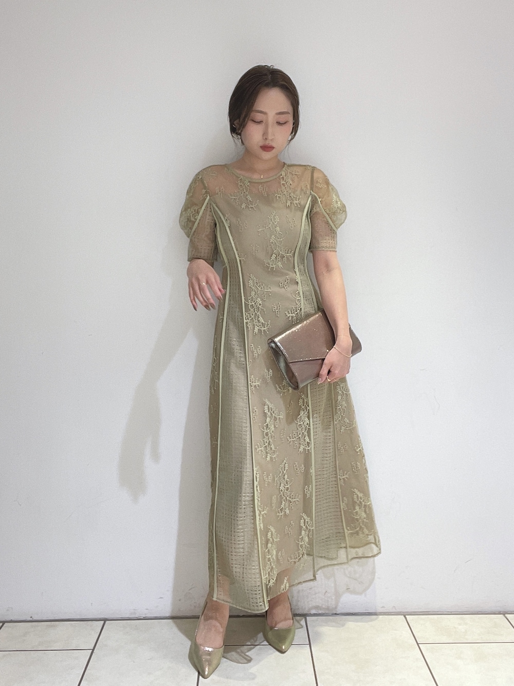 ゴールド系のハンドバッグ、グリーン系のドレス、ゴールド系のパンプスを着用したレディースの冬コーディネートの3枚目の写真