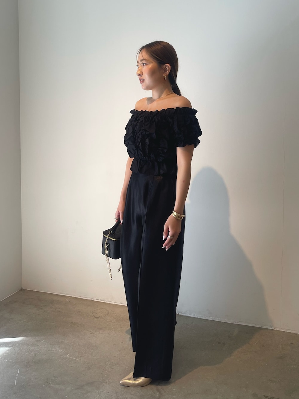 ブラック系のハンドバッグ、ゴールド系のパンプス、ブラック系のパンツドレスを着用したレディースの春コーディネートの5枚目の写真